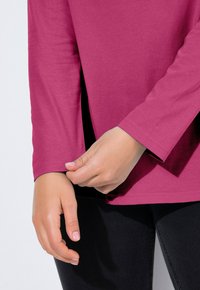 Top z długim rękawem w kolorze magenta, wykonany z miękkiego materiału, o luźnym kroju z rozcięciami po bokach i zaokrąglonym dekoltem.