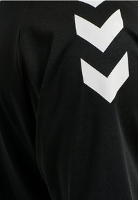 Zwart sportshirt met witte chevronstrepen op de schouder; het materiaal heeft een zachte textuur en een aansluitend ontwerp.