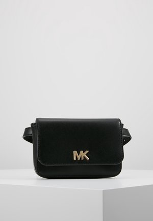 Sac banane en cuir noir avec logo MK doré centré sur le rabat avant, présenté sur un piédestal blanc sur un fond gris clair uni.