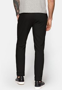 Czarne zwężane spodnie wykonane z gładkiego materiału, z podwiniętymi mankietami i średnim stanem, w połączeniu z eleganckimi czarnymi trampkami.