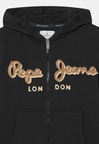 Sudadera con cremallera negra que presenta el bordado "Pepe Jeans" y "LON DON" en beige. Fabricada con un tejido suave, cuenta con un bolsillo frontal y capucha con cordón.