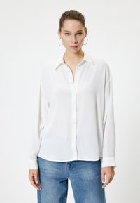 Weißes Hemd mit langen Ärmeln, aus weichem Stoff und mit einem Kragen. Kombiniert mit blauen Jeans im lässigen Schnitt.