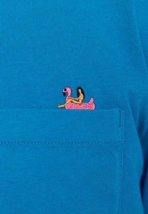 T-shirt bleu avec un design de flottaison en flamant rose brodé sur la poche gauche, avec des accents marron et une texture à côtes fines.