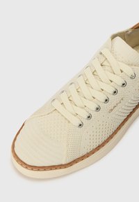 Sneaker beige chiaro realizzato in tessuto testurizzato con sezioni in rete, dotato di lacci rotondi, occhielli in metallo e una suola in gomma color nocciola.