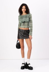 Grønn rutete crop top med snøring, svart lær mini skjørt, kraftige svarte platå sko, og en liten svart håndveske.