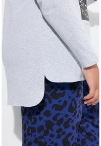 Grijze long-sleeve top met een ronde zoom, gecombineerd met blauwe panty met luipaardprint. De stof lijkt zacht en casual, geschikt voor dagelijks gebruik.
