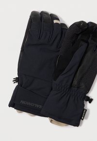 Luvas pretas com uma camada exterior suave e palmas em couro, punho elástico e superfície de aderência texturizada, com um logótipo e faixa ajustável.