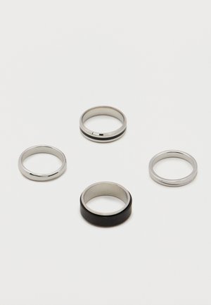 Fire metallringer på en hvit overflate; tre sølvfargede med glatte eller riflete design, en bred med et svart ytre bånd.