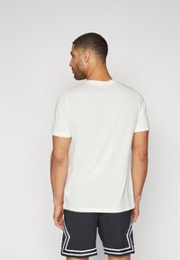 Hvit bomulls t-skjorte med korte ermer og rund hals, brukt med svarte treningsshorts med hvite detaljer og perforert tekstur.
