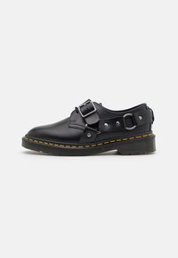 Scarpa in pelle nera con dettaglio a fibbia e cuciture gialle. Presenta una punta arrotondata e una suola in gomma testurizzata per una buona aderenza.