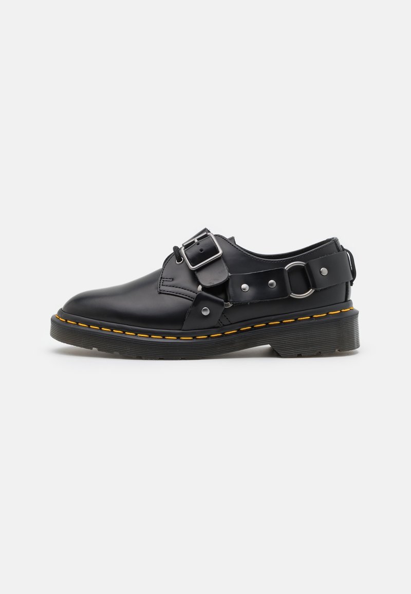 Scarpa in pelle nera con dettaglio a fibbia e cuciture gialle. Presenta una punta arrotondata e una suola in gomma testurizzata per una buona aderenza.
