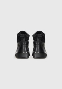 Bottes noires à la cheville avec un extérieur en cuir lisse, des accents en suède, un col rembourré et une semelle en caoutchouc texturée. Fermeture éclair à l'arrière.