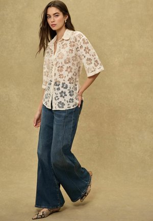 Spitzenknopfleistenhemd in Creme mit Blumenmustern, kombiniert mit weitem dunklem Denim-Jeans und Absatz-Mules im Schlangenledermuster.