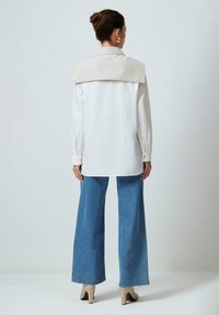 White shirt with a wide beige collar, long sleeves, and button cuffs, paired with light blue wide-leg jeans and beige heels.