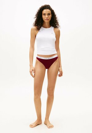 Witte geribde tanktop met een ronde halslijn, gecombineerd met bordeaux rode bikini briefs met een witte merkband. Eenvoudig ontwerp, aansluitende stijl.