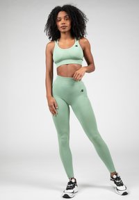 Lichtgroene sportbh en hoge taille legging van rekbaar materiaal. Kenmerkt zich door een strakke uitstraling met subtiele texturen en zwarte logo-accenten.