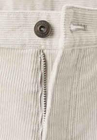 Pantaloni in corduroy grigio chiaro con cerniera argentata e bottone metallico con incisa la scritta "MNG DENIM". Il tessuto presenta una texture a coste verticali.