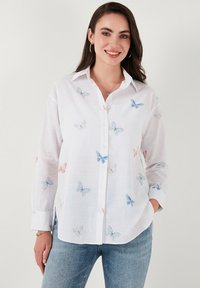 White button-up shirt with long sleeves, featuring colorful butterfly prints in blue and pink, and a textured fabric finish.