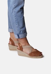 Sandali wedge in pelle intrecciata marrone con cinturini elastici beige, suola in juta e design a punta scoperta. Presentano un motivo intrecciato e testurizzato.