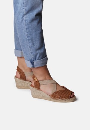 Woven brown leather wedge sandals with beige elastic straps, jute sole, and peep toe design. Features a textured, braided pattern.