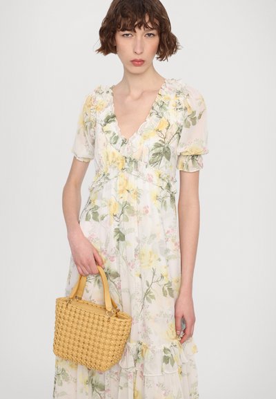 Bloemrijke maxi-jurk met gele en groene patronen, gerimpelde V-hals en mouwen. Houdt een kleine gele gehaakte handtas met korte hengsels vast.