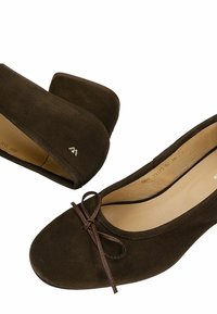 Ballerines en suede marron avec des orteils ronds, un détail de nœud marron et un petit talon, présentant un logo discret sur le côté.