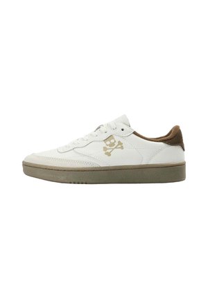 Zapatilla blanca de corte bajo con suela beige, forro interior marrón y un pequeño logo beige de calavera y huesos cruzados en el lateral.