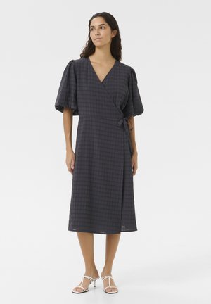 Robe enveloppante à carreaux gris, avec de courtes manches bouffantes, longueur cheville, détail noué à la taille, fabriquée en tissu texturé. Assortie avec des sandales blanches.