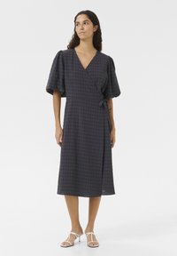 Anglies spalvos languota apdaras su trumpomis pūstomis rankovėmis, juosmens surišimo detale ir vidutinio ilgio sijonu. Pagaminta iš tekstūruoto audinio.