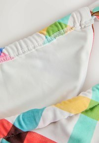 Kolorowy, wzorzysty top od bikini z elastyczną białą podszewką. Posiada marszczoną elastyczną opaskę z geometrycznymi kształtami w kolorach różowym, niebieskim i żółtym.