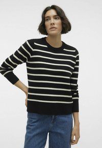 Pull noir et crème à rayures avec un col rond et des manches longues, associé à un jean taille haute bleu. Texture douce, coupe décontractée.