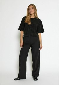 Juodas tekstūruotas trumpas rankovės marškinėlis derinamas su juodais plačiais kelnais. Apranga turi lygią apdailą ir švarų dizainą, kuriame yra subtilių raštų.