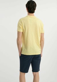 Jasnożółta koszulka z krótkim rękawem wykonana z miękkiego materiału, w połączeniu z granatowymi szortami. Koszulka ma klasyczny okrągły dekolt i luźny krój.