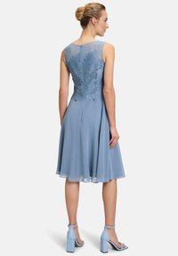 AINE Kleid in Hellblau mit einem engen Spitzenoberteil, das Blattformen aufweist, einem fließenden Rock und einem Reißverschluss auf der Rückseite. Passende blaue Blockabsätze.