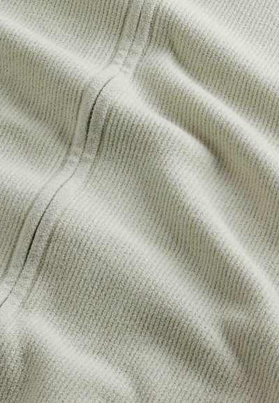 Hellgrauer Stoff mit einer strukturierten, gerippten Oberfläche. Das Material wirkt weich und plüschig, mit sichtbaren Nähten.