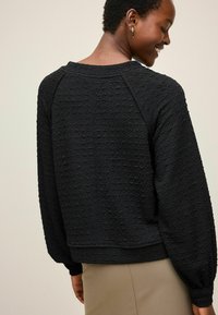 Zwarte textured sweatshirt met een ronde hals, raglanmouwen en een cropped pasvorm, gecombineerd met een beige onderstuk.