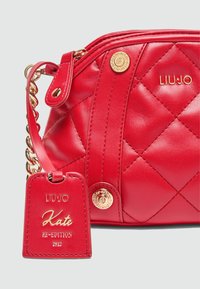 Rote gesteppte Leder-Schultertasche mit goldenen Hardware, eingeprägtem Logo und einem abnehmbaren Anhänger, der "Kate RE-EDITION 2012" zeigt.