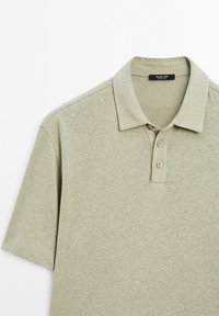 Polo a maniche corte di colore verde oliva chiaro, realizzato in tessuto morbido. Presenta un colletto, una chiusura a tre bottoni e una texture delicata.