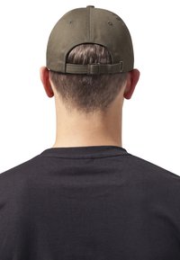 Olivenfarvet justerbar kasket med rund krone og stofrem bagpå, båret af en person i sort skjorte, set fra bagenden.
