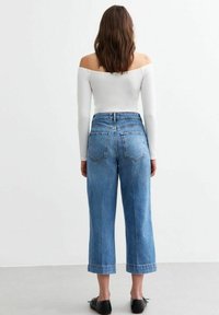 Jeans de mezclilla azul de talle alto y pierna recta con dobladillo enrollado, con bolsillos traseros y lavado claro, combinados con una camiseta blanca ajustada.