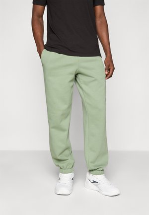 Lichtgroene sweatpants van zacht materiaal, met elastische boorden, zijzakken en een relaxte pasvorm, gecombineerd met witte sportschoenen.