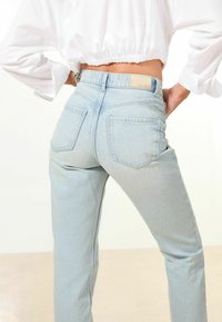 Jeans in denim azzurro chiaro con vita alta, dotati di tasche posteriori e leggere sfumature. Il tessuto ha una finitura leggermente testurizzata.