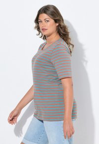 Camiseta a rayas en marrón con líneas turquesas, de mangas cortas, con cuello redondo y un corte relajado. Combinada con pantalones cortos de mezclilla claros.