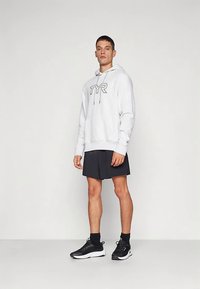 Ανοιχτό γκρι φούτερ με κορδόνι και λογότυπο TYR, σε συνδυασμό με μαύρα αθλητικά σορτς, μαύρες κάλτσες και μαύρα αθλητικά παπούτσια.