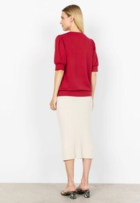 Top rosso a maniche corte con maniche a sbuffo, abbinato a una gonna midi a coste beige. Sandali neri con tacco e motivo in pelle di serpente.