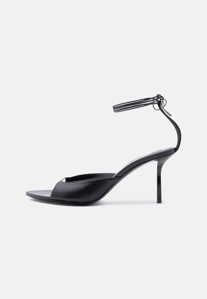 Μαύρο δερμάτινο σανδάλι στιλέτο με λεπτό λουράκι αστραγάλου, ανοιχτό δάχτυλο και μέτρια ψηλό τακούνι σε λευκό φόντο.