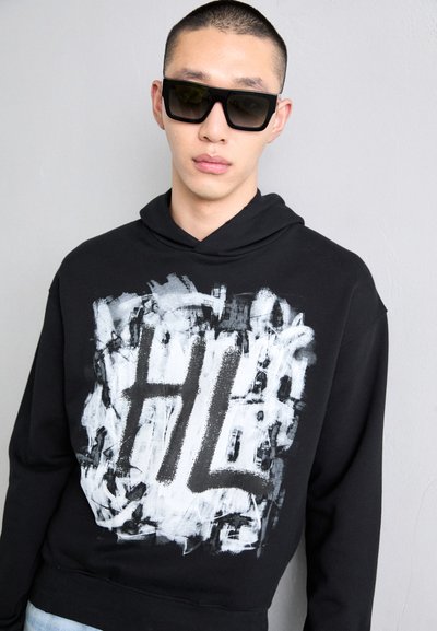 Sudadera negra con un gran diseño abstracto en blanco y gris que presenta "HL". La tela parece suave, con capucha ajustable y un corte holgado.