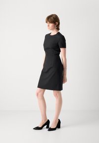 Black fitted dress with short sleeves, round neckline, and a tailored silhouette. Paired with black pointed-toe heels. Smooth fabric texture.