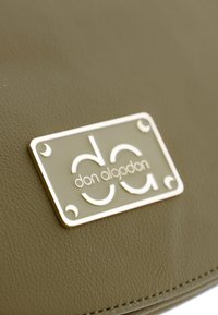 Bolso de cuero verde oliva con superficie texturizada, que presenta una placa de logo plateada que muestra "don algodón" y un diseño distintivo.