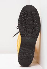 Botte en caoutchouc jaune avec une semelle texturée noire. Elle est dotée de lacets et d'une surface supérieure lisse. La semelle présente un motif pour une meilleure adhérence.